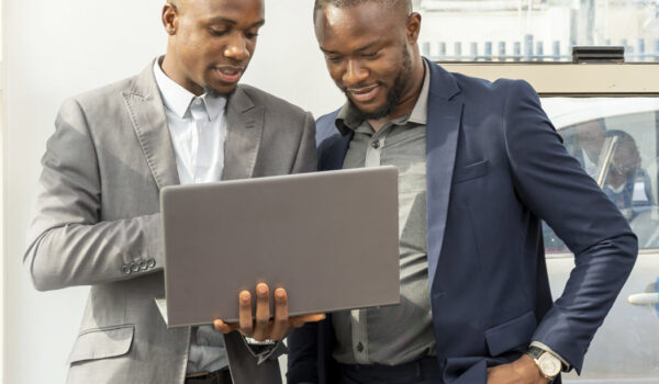 Young black businessmen standing together holding a laptop, disc